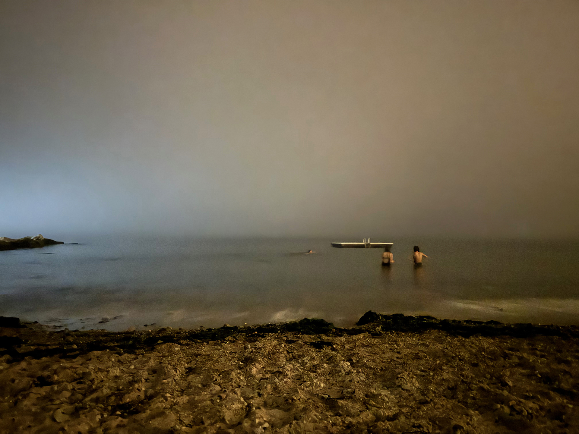 Photograph of two figures wading in the waves, girls in water, searching, night, looking in the sea, going towards the float, and a swimmer in the water, disappearing figures, sand, beach, night scene, dreamlike landscape