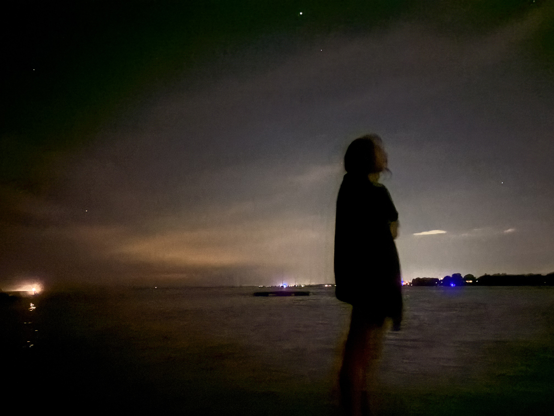 A girl standing in the waves at night looking up to the stars dreaming